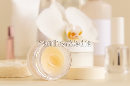 Smass opened Glass jar and other cosmetics near white orchid flower on light beige close up. Beauty products for everyday woman face care routine,  Exotic Spa Treatments