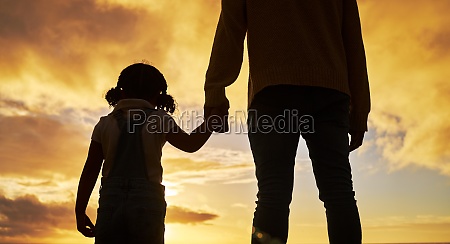 Sunset,  silhouette and father holding hands with child at the beach standing together. Love,  affection and dad bonding with girl by ocean enjoying holiday,  family vacation and weekend in summer.