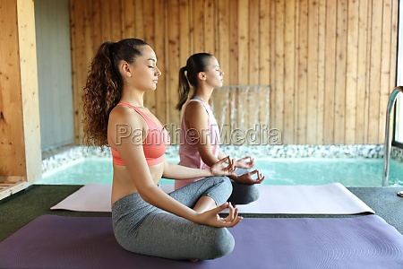 Two women doing yoga exercises in spa near a pool