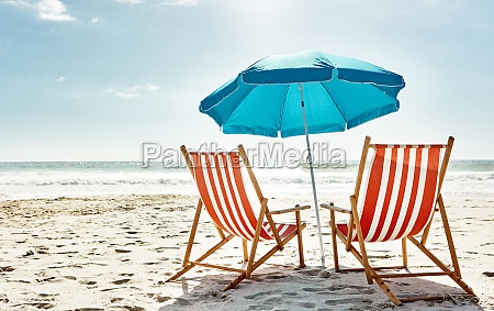 Get some summer in your life. Still life shot of two deck chairs under an umbrella on the beach