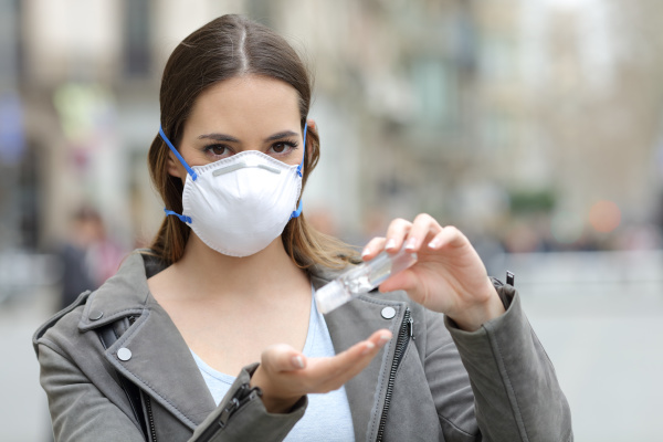 mujer con mascara protectora usando desinfectante
